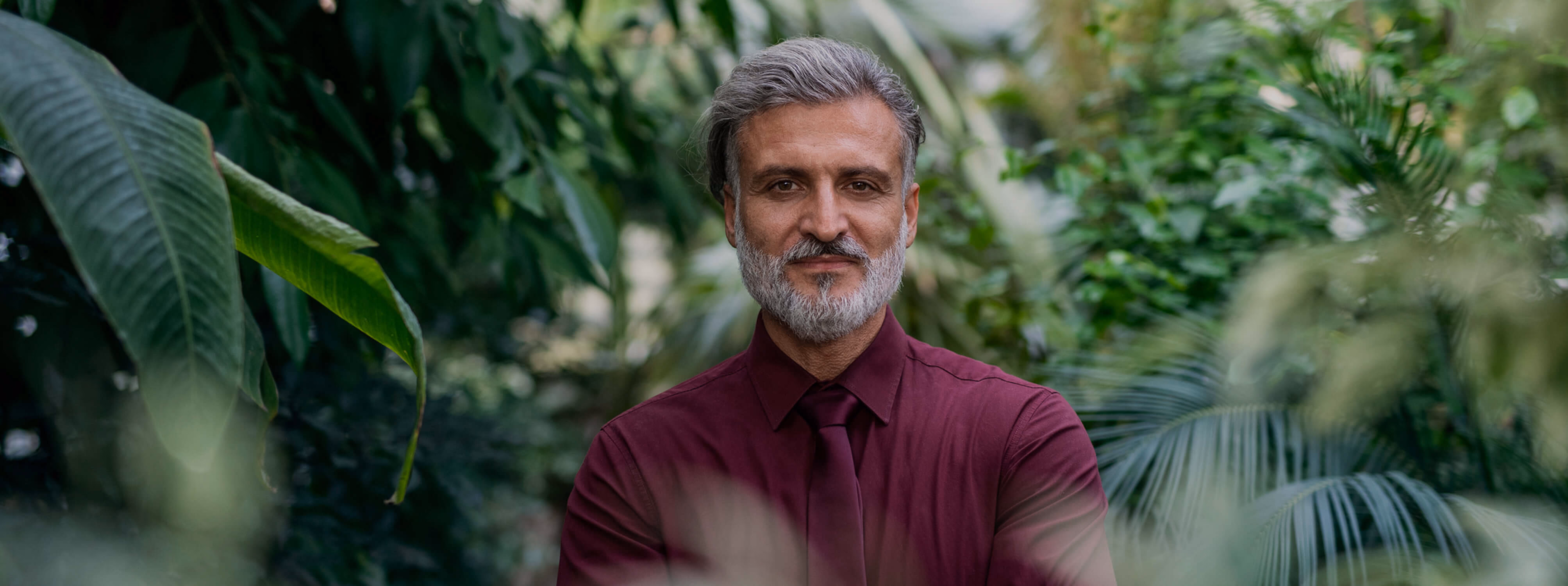 Mature man with gray beard surrounded by lush green tropical plants